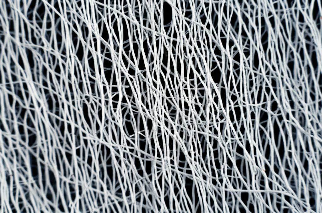 Ảnh chụp hiển vi (microscopic) cấu trúc sợi microfiber, thể hiện rõ các sợi siêu nhỏ và khoảng trống giữa các sợi. Chú thích rõ ràng về cấu trúc.
